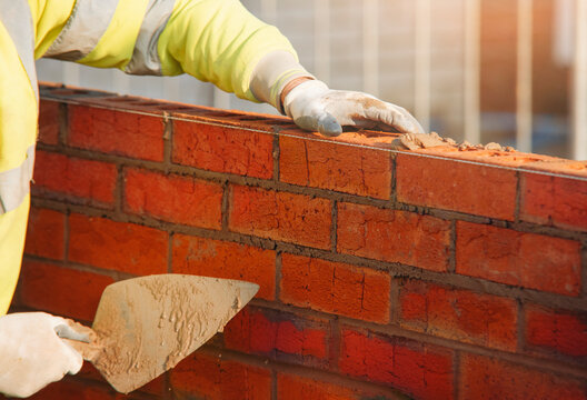 Mason lays red bricks on a wall at a construction site
