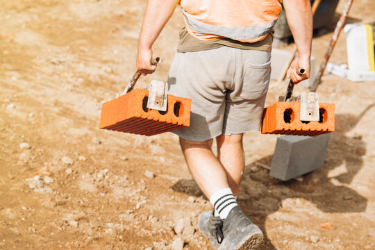 Construction worker carries two bricks across a building site