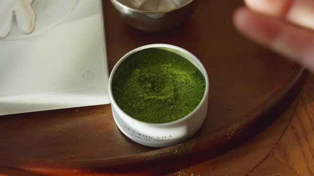 Scooping matcha powder from a tin with a metal spatula