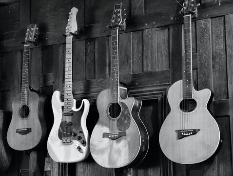 Monochrome view of acoustic and electric guitars hanging on a dark wooden wall. Ideal for music studio, instrument store, vintage poster, concert, retro style, and fine art concepts.
