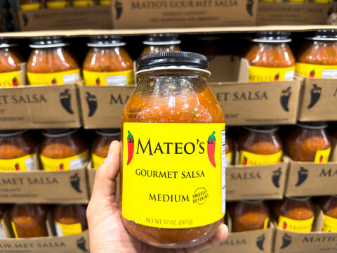 Prosper, Texas, USA - September 21st, 2026: Person holding Mateo's gourmet salsa medium glass jar with yellow label in Costco store