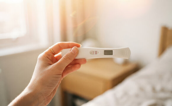 Woman holding a positive pregnancy test in bedroom, concept of family planning, motherhood, and fertility testing for young adult female