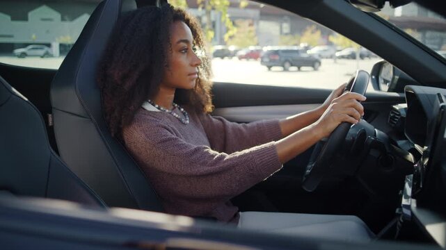 Focused woman sits behind steering wheel inside parked car