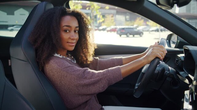 Smiling woman looks happily while sitting inside parked own car