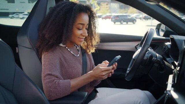 Woman checks smartphone while sitting in driver seat in car