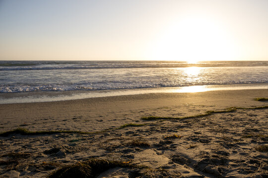 A beautiful scenic view of Pacific Beach in San Diego California during a warm glowing sunset with waves crashing onto sandy shore, San Diego, CA