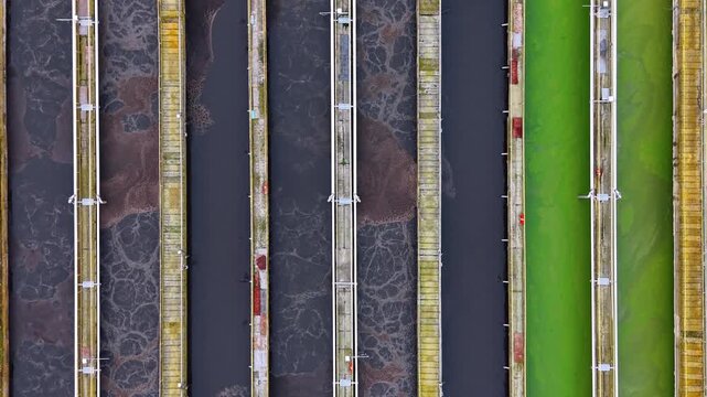Overhead view of aeration tanks and algae basin at treatment plant. An aerial perspective shows vertical concrete walkways separating bubbling wastewater from green liquid.