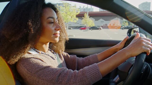 Focused woman drives modern car through sunny city streets