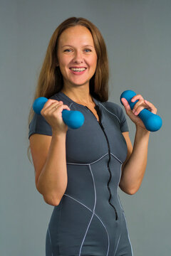 Confident female Pilates instructor in a relaxed professional pose holding small dumbbells, lifting both weights in a biceps curl