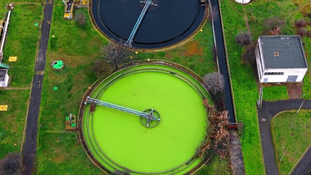 Circular clarifier with green water top down aerial view. A top down perspective shows a round concrete tank filled with bright green water and a rotating metallic arm.