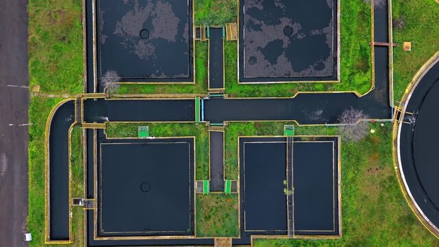Top down drone shot of rectangular sedimentation tanks at treatment plant. Overhead camera captures dark water channels and rectangular pools surrounded by yellow railings.