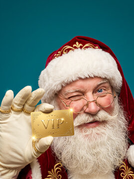 Santa Claus winking and holding a gold VIP membership card, festive red and white hat with embroidery, celebratory mood. Holiday, luxury, marketing, advertising.