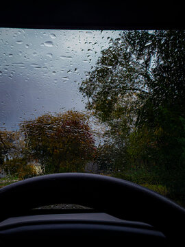 Raindrops covering a vehicle windshield on a gloomy stormy autumn day viewed from inside behind the steering wheel