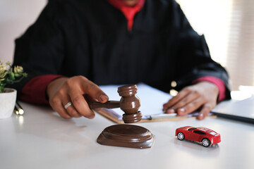 A close-up shot of a judge striking a gavel on a courtroom desk, with a miniature car model placed beside it. This image represents legal issues related to car ownership, pawn transactions, sales, ins © PANCASONA CREATION