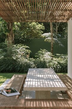 Limestone outdoor dining table beneath slatted teak pergola in tropical garden setting