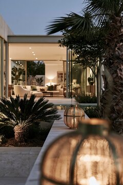 Glowing brass lantern framing modern glass house at blue hour in tropical garden courtyard