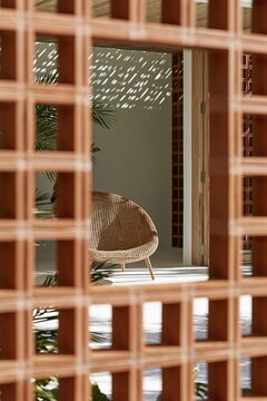 Woven cane armchair viewed through terracotta screen on shaded modern verandah