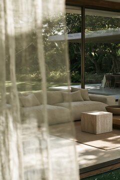 Sand linen sectional sofa seen through sheer curtain in glass walled modern living room