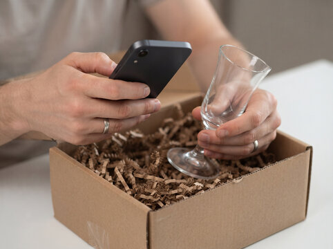 Person holding a smartphone and a broken glass wine goblet from a delivery package box