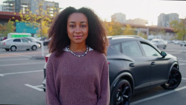 Cheerful African American woman stands near parked vehicle
