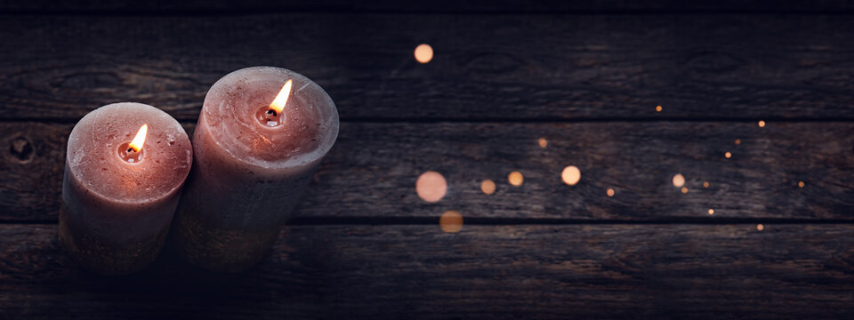 Two burning candles with magical bokeh lights on old wooden table. Horizontal top view photography with copy space. Perfect for special moments.