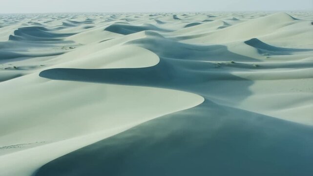 Pale sand dunes extend across a vast desert landscape beneath a hazy open sky