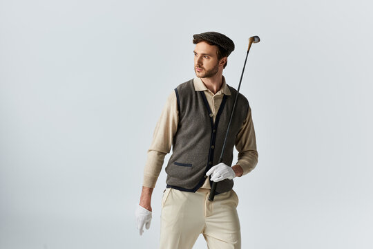 Bearded gentleman in tweed and flat cap poses with a golf club in a bright studio