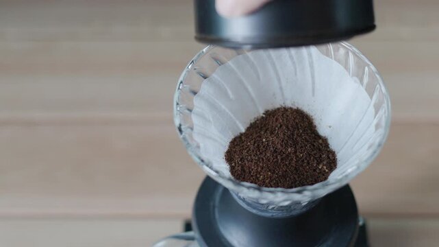 Ground coffee, close up of ground coffee in white paper filter inside ribbed glass cone dripper on black base before pour over brewing method