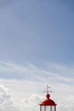 Red weather vane beneath expansive blue sky in Portugal