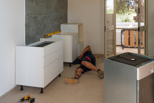 Handyman lying on floor to install new kitchen cabinets in a New Home