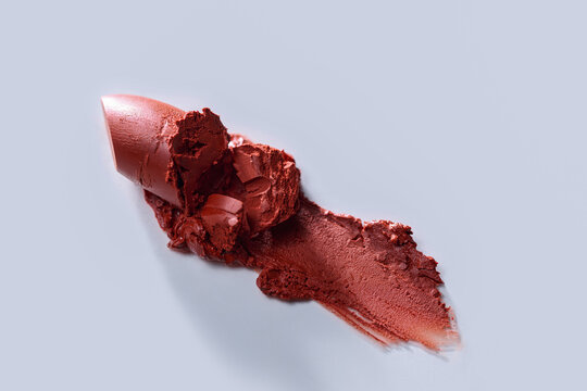 Lipstick smear and broken lipstick on a white surface.