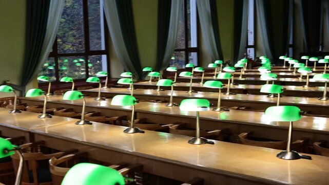 Empty historic library reading room with green banker lamps on wooden desks by autumn windows