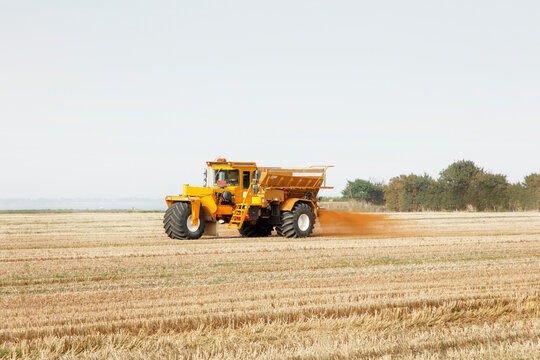 Yellow Fertilizer Spreader Tractor Spreading Soil Amendment Over Harvested Field In Rural Countryside