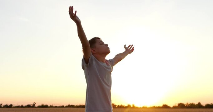Boy raises arms toward sunset in open field, expressing freedom and hope. Golden horizon creates peaceful inspiring mood. Outdoor footage supports dreams, optimism, and motivational storytelling.