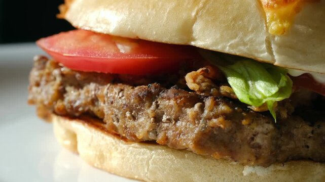 Delicious beef burger resting quietly on white reflective surface displaying grilled patty melted cheese fresh tomato green lettuce, toasted bun under studio light. Freshly cooked beef burger on plate