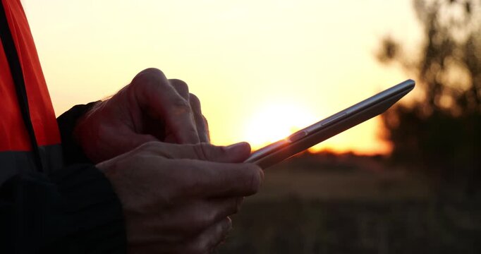Industrial engineer uses tablet at sunset. He enters data, analyzes results, and manages field operations. Warm evening light creates digital workflow for industrial monitoring and control. Close-up.