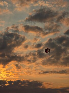 Parasailing parachute flying in a dramatic sunset sky with orange clouds