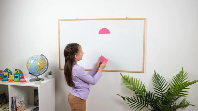 In 4K, a school age girl places magnetic half circle pieces on a whiteboard during a math lesson, using a visual fraction model to understand halves and equal parts.