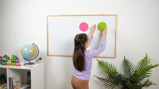 4K, a girl writes a math symbol between magnetic fraction circles on a classroom whiteboard, practicing fraction comparison and visual representation with colorful learning aids.