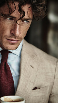 Close-up portrait of a man with blue eyes, brown curly hair, wearing a blue striped shirt and a burgundy tie, showcasing a sophisticated and thoughtful expression, symbolic of refinement and intellect