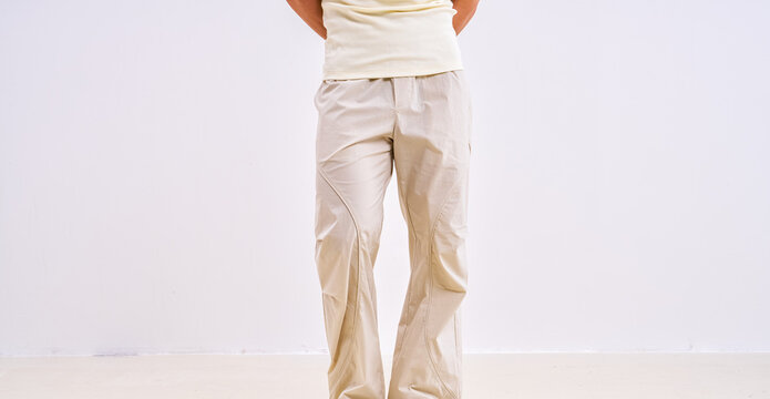Athletic Asian male model wearing beige casual cargo trousers, studio apparel photography on plain light background