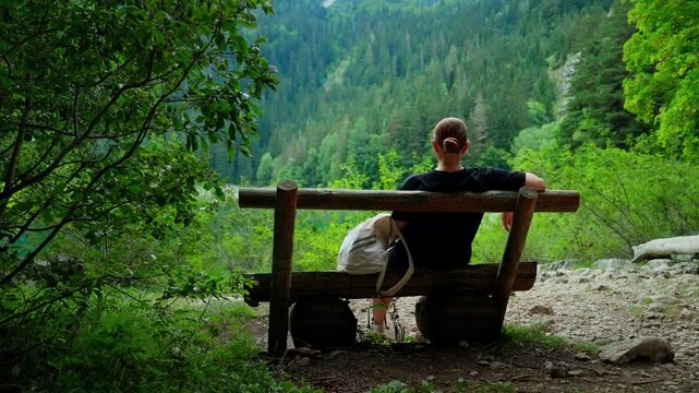 Woman resting on rustic wooden bench overlooking lush green forest valley, enjoying peaceful solitude and tranquil nature scenery during a quiet outdoor escape