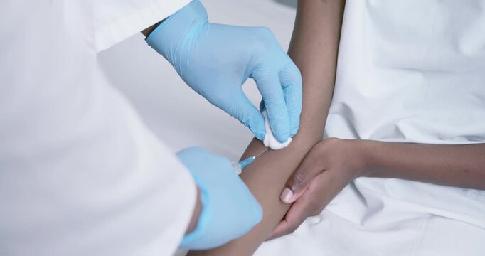 Clinician is pressing cotton pad, aligning syringe, inserting needle into vein to collect blood