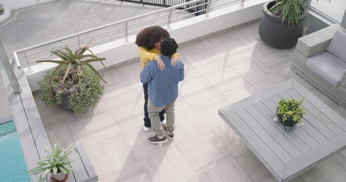 Facing railing together, African American couple dancing and embracing on tiled terrace, in love