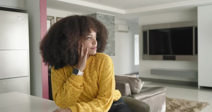 African American woman in mustard sweater leaning at kitchen counter, smiling as lens zooming