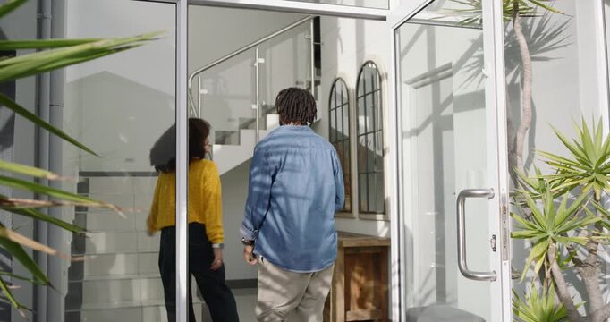 African American couple returning home at front entry, man opening glass door, handing keys