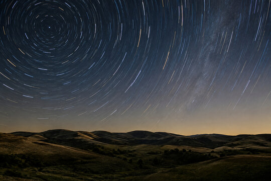 丸みのある丘陵の上空に小さな円形の星の軌跡が巡る夜景