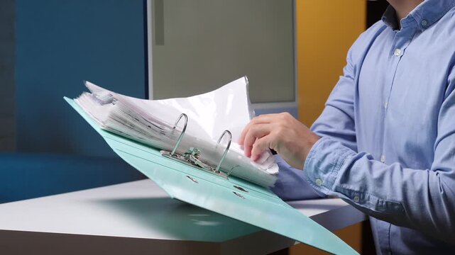 Businessman sorting office documents in an open ring binder, organizing paperwork and administrative records at a desk in a modern workplace for efficient filing and business administration