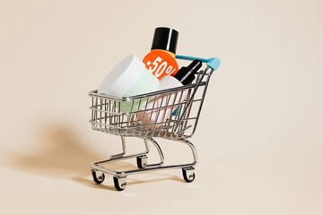Small metal shopping cart filled with cosmetic bottles and a discount tag on beige background © Sajida