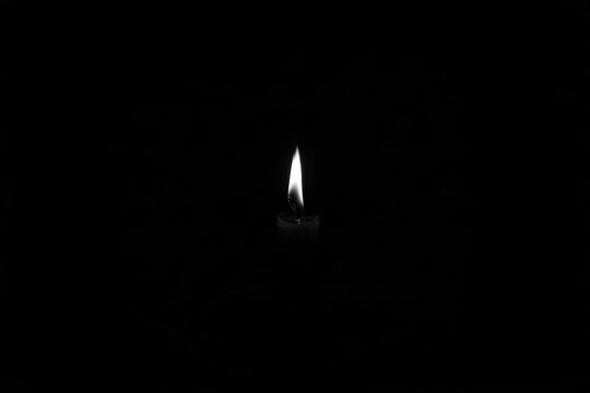 a single bright candle flame glows in the dark against a black background